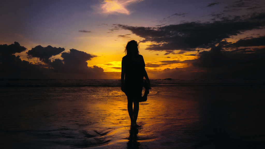 Image of woman standing in front of sun setting at beach